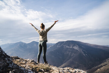 Young cheering woman hiker open arms at mountain peak cliff, fitness girl hiker enjoy the view on mountain top, hiker standing with hands up achieving the top, women enjoy freedom