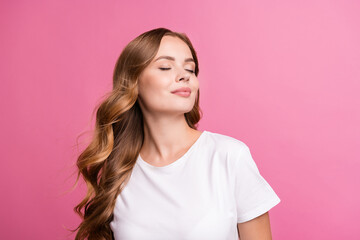 Fototapeta premium Portrait of peaceful girl with fluttering curly hair dressed white t-shirt close eyes enjoy wind blow isolated on pink color background