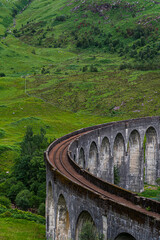 Obraz premium Traversing the Highland Rails: Stone Bridge Arching Over a Picturesque Scottish Valley Amidst Majestic Highlands