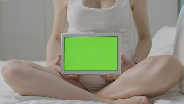Pregnant woman Expecting mother seated with tablet, green chroma key screen ready for customize content, screen replacement mockup. Perfect for targeted advertising and family-focused application.