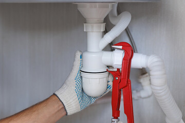 Close up of professional plumber installs a siphon pipe on the kitchen sink.