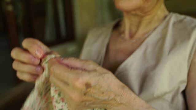 Close-up of a fingers caucasian elderly woman sews by hand with a needle and thread. Selective focus.
