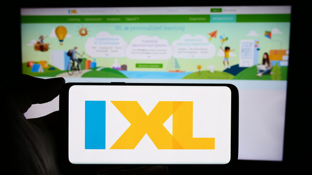 Stuttgart, Germany - 02-08-2024: Person holding mobile phone with logo of American online education company IXL Learning Inc. in front of web page. Focus on phone display.