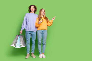 Full body portrait of two astonished youngsters hold smart phone mall bags indicate finger empty...