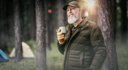 Homme aventurier quinquagénaire qui fait du camping et une randonnée dans la nature avec une tente et qui boit une tasse de café