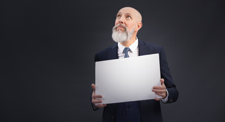 Portrait corporate d'un homme d'affaires en costume et avec barbe qui tient un panneau affiche blanc et qui regarde en l'air