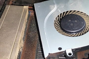 Dismantled parts of an old laptop, cooling systems, like a fan and a radiator, which are clogged with dust and lint. Consequences of using a laptop while lying or sitting on the couch on laps