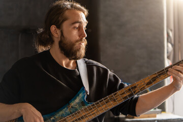 Man with beard plays bass guitar. His fingers move quickly along the strings, creating music....