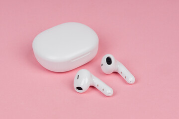 White wireless headphones on pink background. New earphones. New technologies.