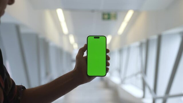 4K caucasian man show the Green Screen phone in aisle with columns. Using Smartphone for one advertisement