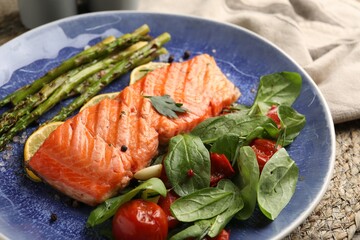 Tasty grilled salmon with tomatoes, asparagus, spinach and spices on table, closeup