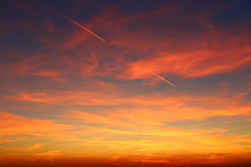 airplane and its trail in the sky. clouds and different color tones in the sky at sunset. Amazing and incredible sunset.