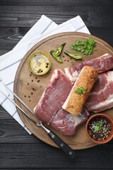 Pieces of raw pork belly, chili pepper, peppercorns, oil and parsley on black wooden table, top view