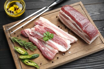 Pieces of raw pork belly, chili pepper, peppercorns, rosemary and parsley on black wooden table, above view