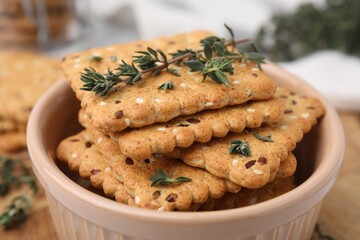 Cereal crackers with flax, sesame seeds and thyme in bowl on blurred background, closeup