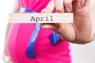 Pregnant woman in pink dress with blue ribbon showing word april. Expecting for newborn and expansion of family