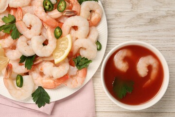 Tasty boiled shrimps with cocktail sauce, chili, parsley and lemon on light wooden table, flat lay