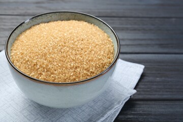 Brown sugar in bowl on black wooden table, closeup