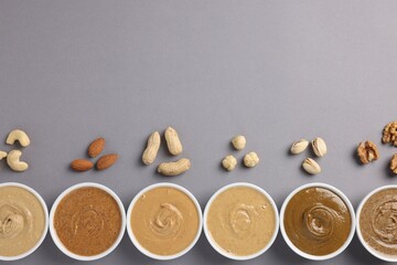 Many tasty nut butters in bowls and nuts on grey table, flat lay. Space for text