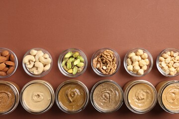 Many tasty nut butters in jars and nuts on brown table, flat lay. Space for text