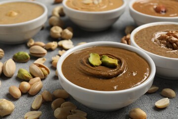 Tasty nut butters in bowls and raw nuts on light grey table, closeup