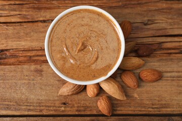 Delicious nut butter in bowl and almonds on wooden table, top view