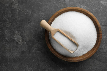 Granulated sugar in bowl and scoop on grey textured table, top view. Space for text
