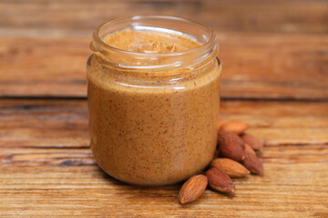 Tasty nut paste in jar and almonds on wooden table, closeup