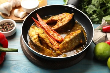 Tasty fish curry in frying pan and ingredients on light blue wooden table, closeup. Indian cuisine