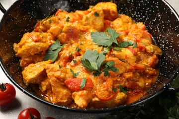 Delicious chicken curry in frying pan and tomatoes on table, closeup