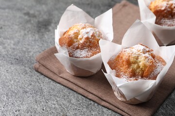 Delicious muffins with powdered sugar on grey table, closeup