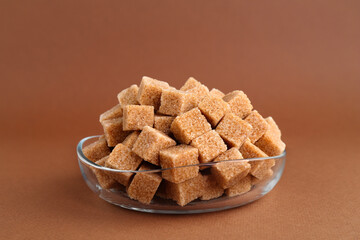 Brown sugar cubes in bowl on color background, closeup
