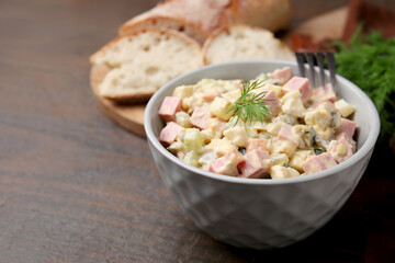 Tasty Olivier salad with boiled sausage in bowl on wooden table, space for text