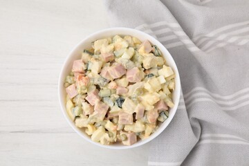 Tasty Olivier salad with boiled sausage in bowl on white wooden table, top view