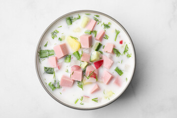 Delicious cold summer soup (okroshka) with boiled sausage in bowl on white table, top view