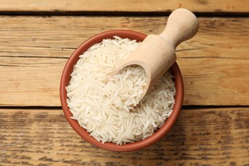 Raw basmati rice and scoop in bowl on wooden table, top view
