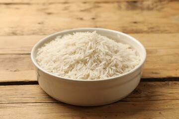 Raw basmati rice in bowl on wooden table, closeup