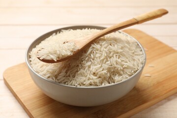 Fototapeta na wymiar Raw basmati rice and spoon in bowl on white wooden table