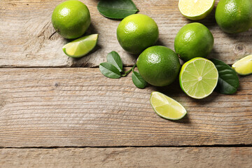Fresh limes and green leaves on wooden table, flat lay. Space for text