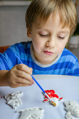 The kid draws and paints plaster figures with a brush and gouache on a piece of paper.