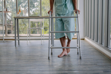 Caucasian male practice walking slowly with walker in hospital. Focus on legs young man injuries...