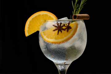 Gin and tonic cocktail with orange, cinnamon, rosemary and star anise on a black background