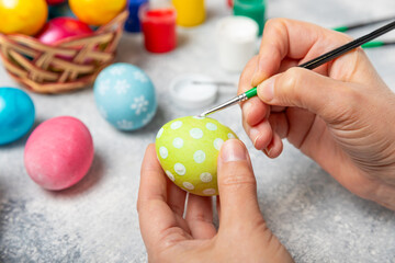 Woman paints Easter eggs at the kitchen wooden table.Happy Easter celebration concept.Colorful Easter eggs with different patterns.Paints,decorations for coloring eggs for holiday.Creative background.