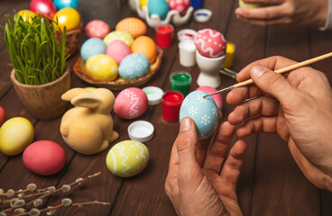 Man paints Easter eggs at the kitchen wooden table.Happy Easter celebration concept.Colorful Easter...