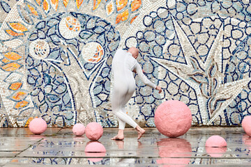 Young hairless girl ballerina with alopecia in white futuristic suit dancing outdoor among pink...