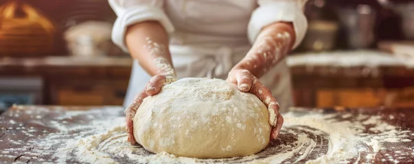 Fototapeten A baker kneads dough preparing it for baking fresh bread against blurred bakery background.  © julijadmi