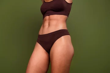 Gordijnen Cropped no retouch photo of sexual beautiful woman with strong mascular athletic body abs isolated on khaki color background © deagreez