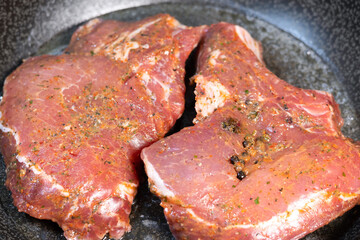 Delicious juicy pork steak seasoned with rosemary and garlic is fried in a pan.