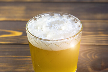 Gold-yellow beer with white foam into a glass. Close up view.