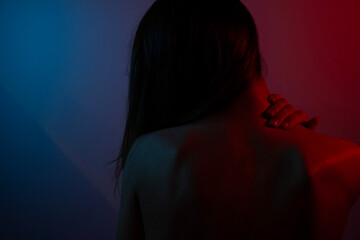 Intense young woman, blue and red lighting on back. Neck and back pain.Mental burden concept